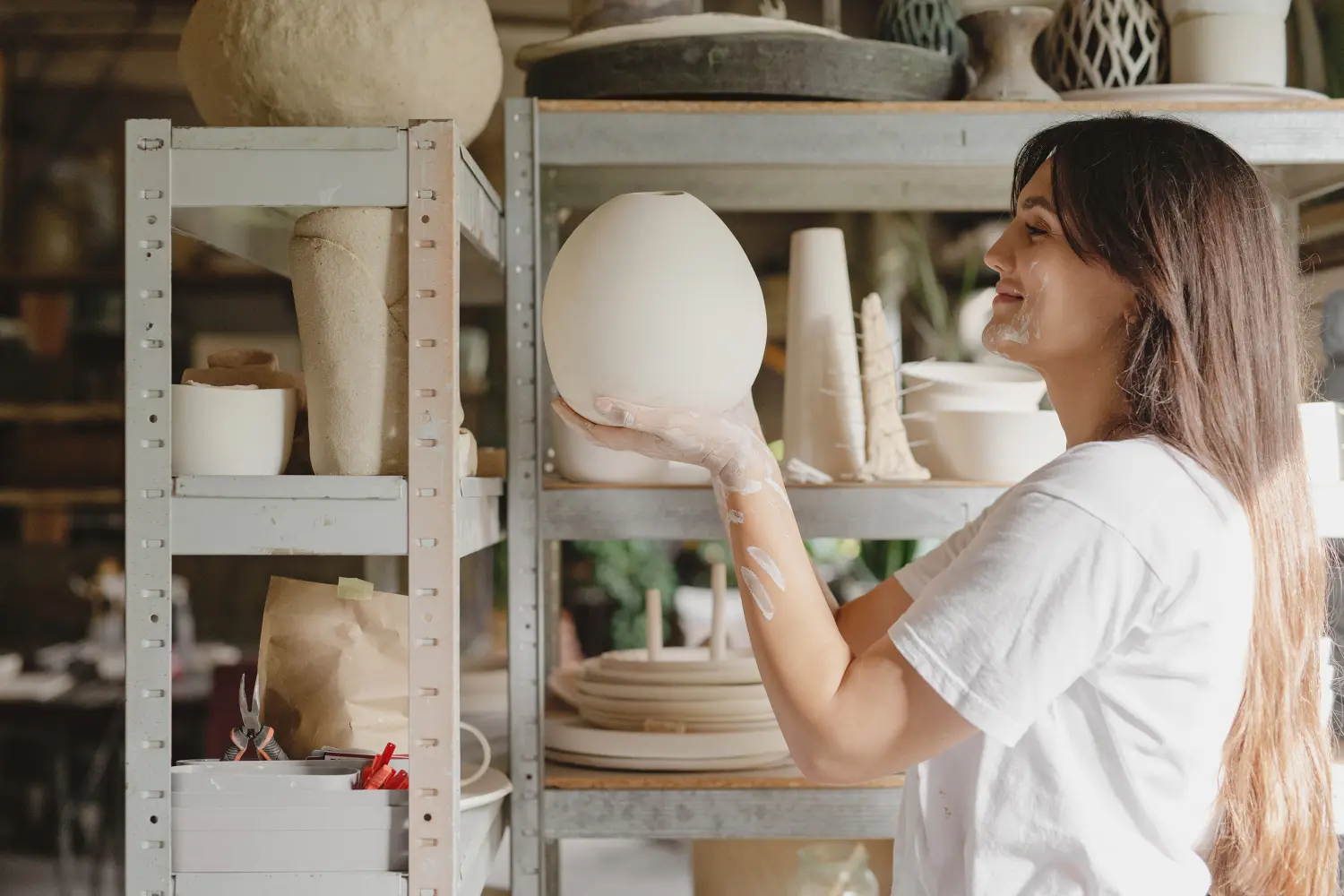 A woman in a ceramic studio holding a handcrafted vase, representing creativity and craftsmanship.