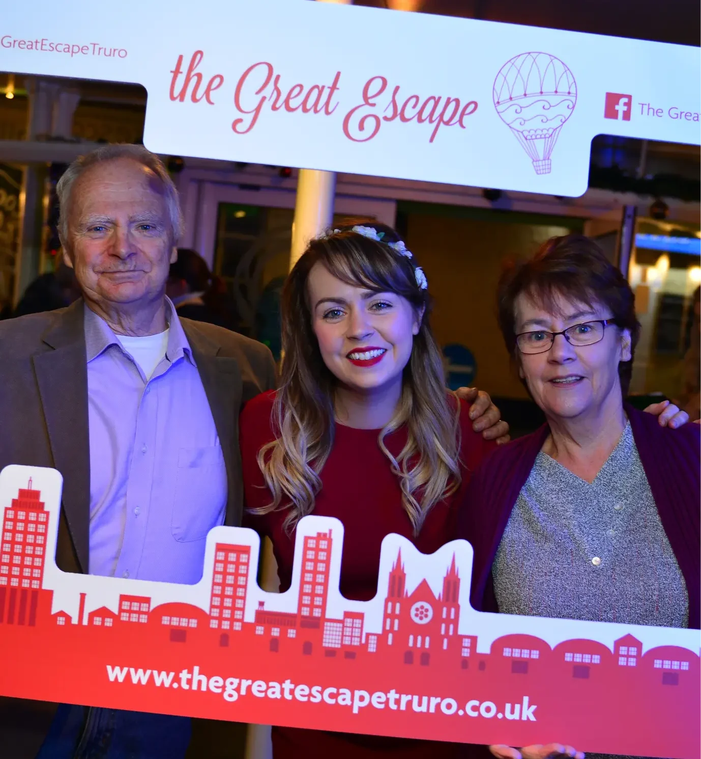 A group photo featuring three people holding a colourful "The Great Escape Truro" sign at an event.