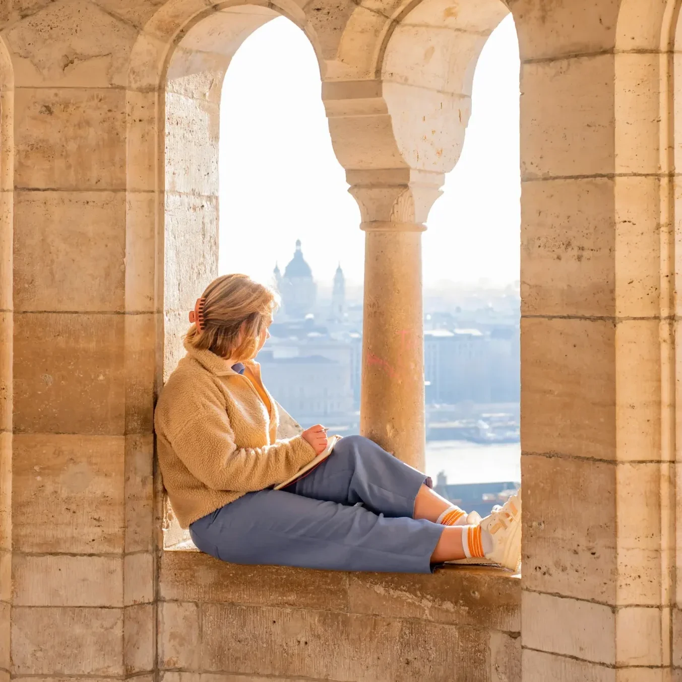 A website copywriter sitting in a stone archway at Fisherman’s Bastion, looking out at Budapest.