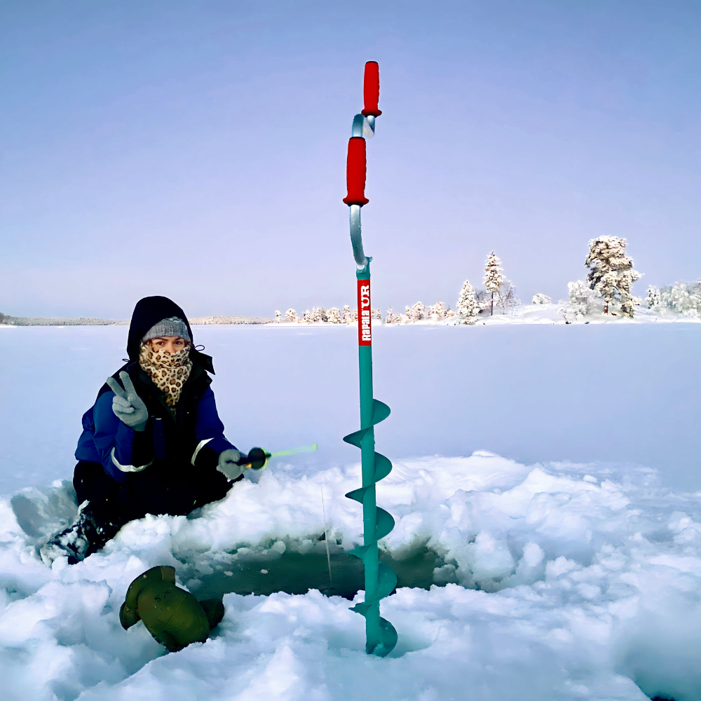 A freelance travel writer sat on a frozen lake holding up a peace sign with one hand while ice fishing with the other.