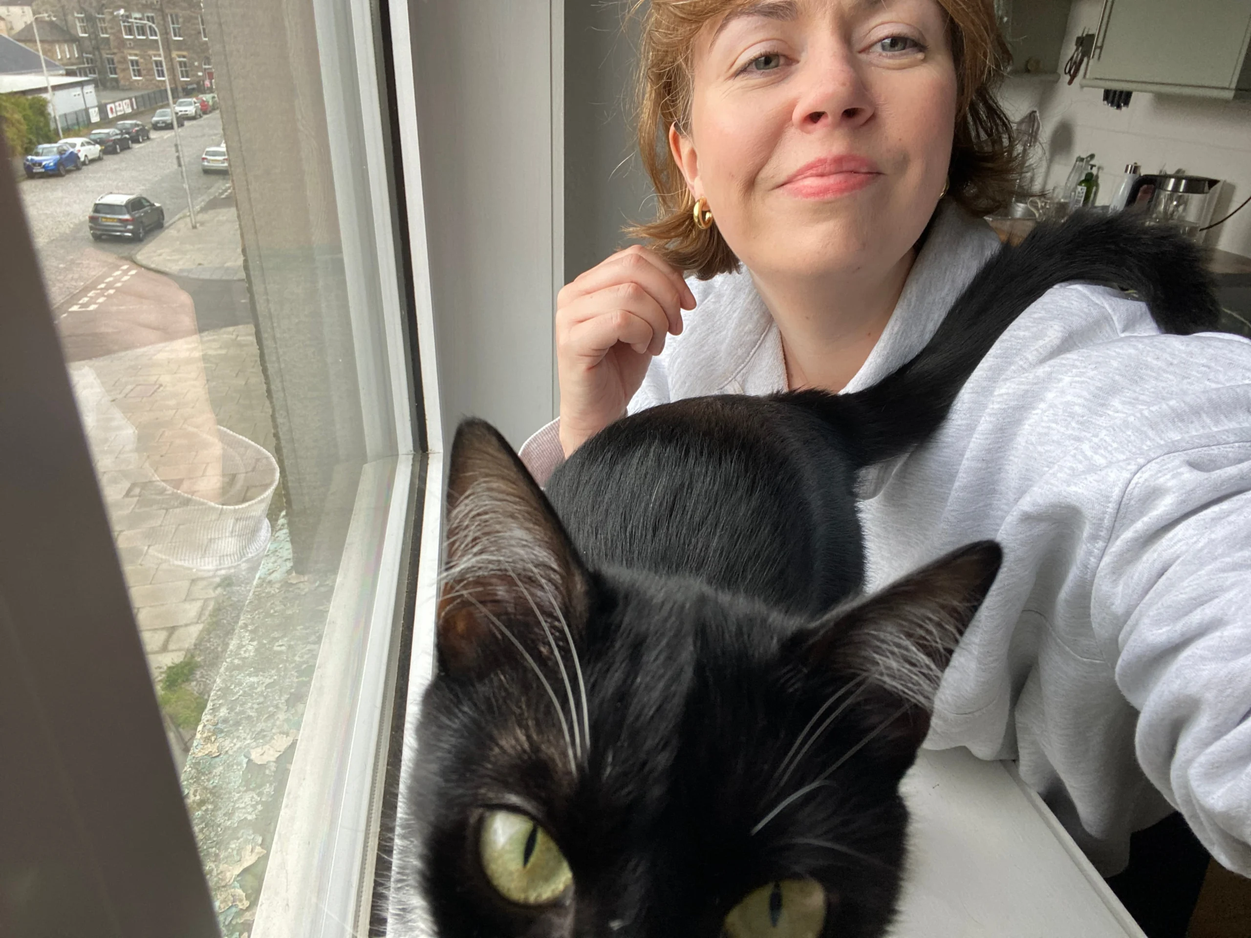 Woman smiling with a black cat sitting close to the window, capturing a moment during a house sit.