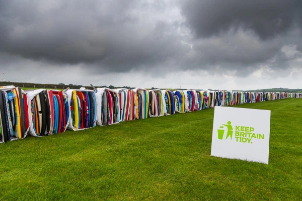 Demonstrating beach pollution with long line of colourful surfboards against stormy sky with Keep Britain Tidy sign