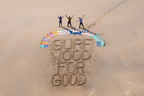 Aerial view of "surf wood for good" written in sand with wooden bellyboards and people posing, spreading awareness of beach pollution