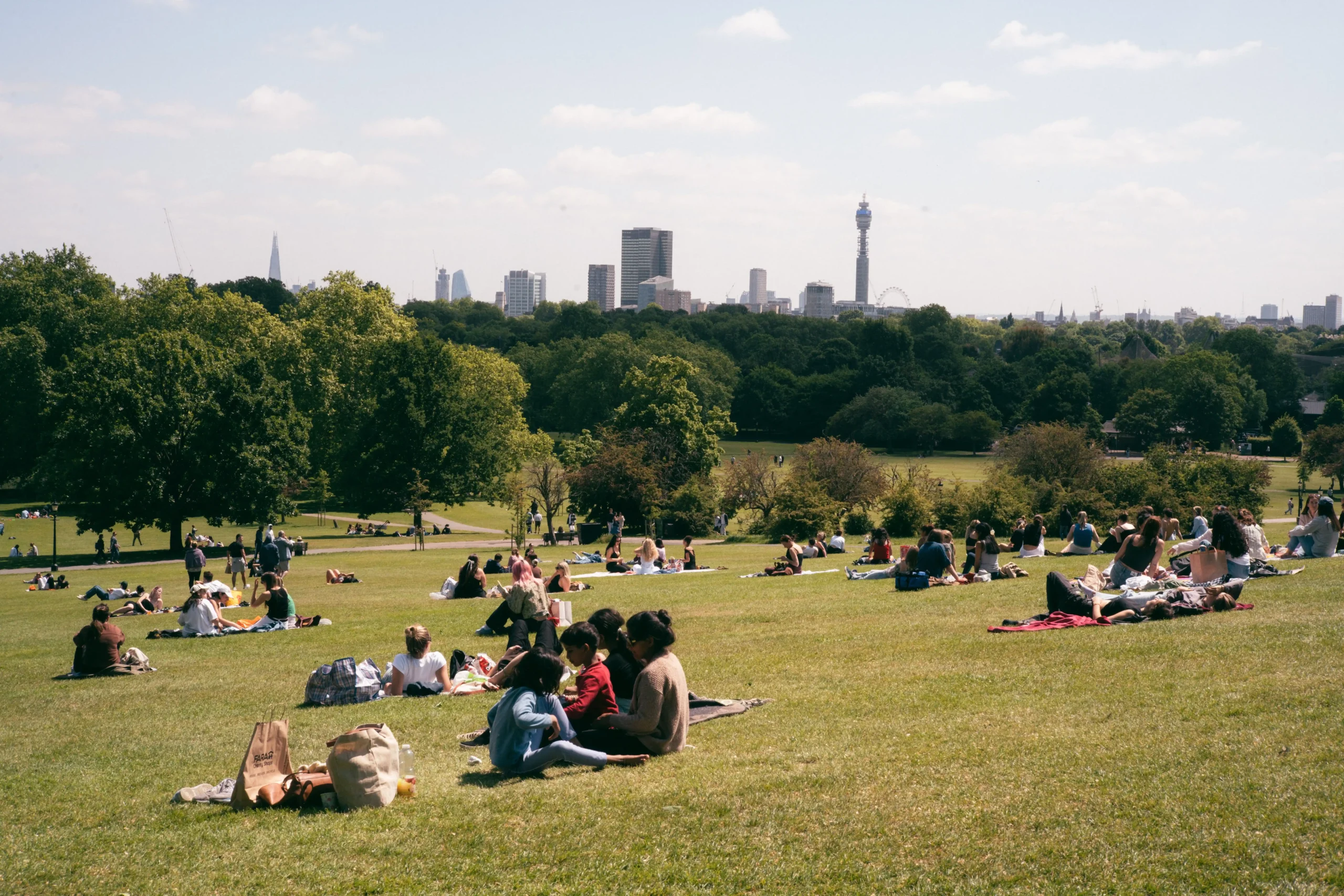 People relaxing on Primrose Hill with a view of the London skyline on a sunny day.