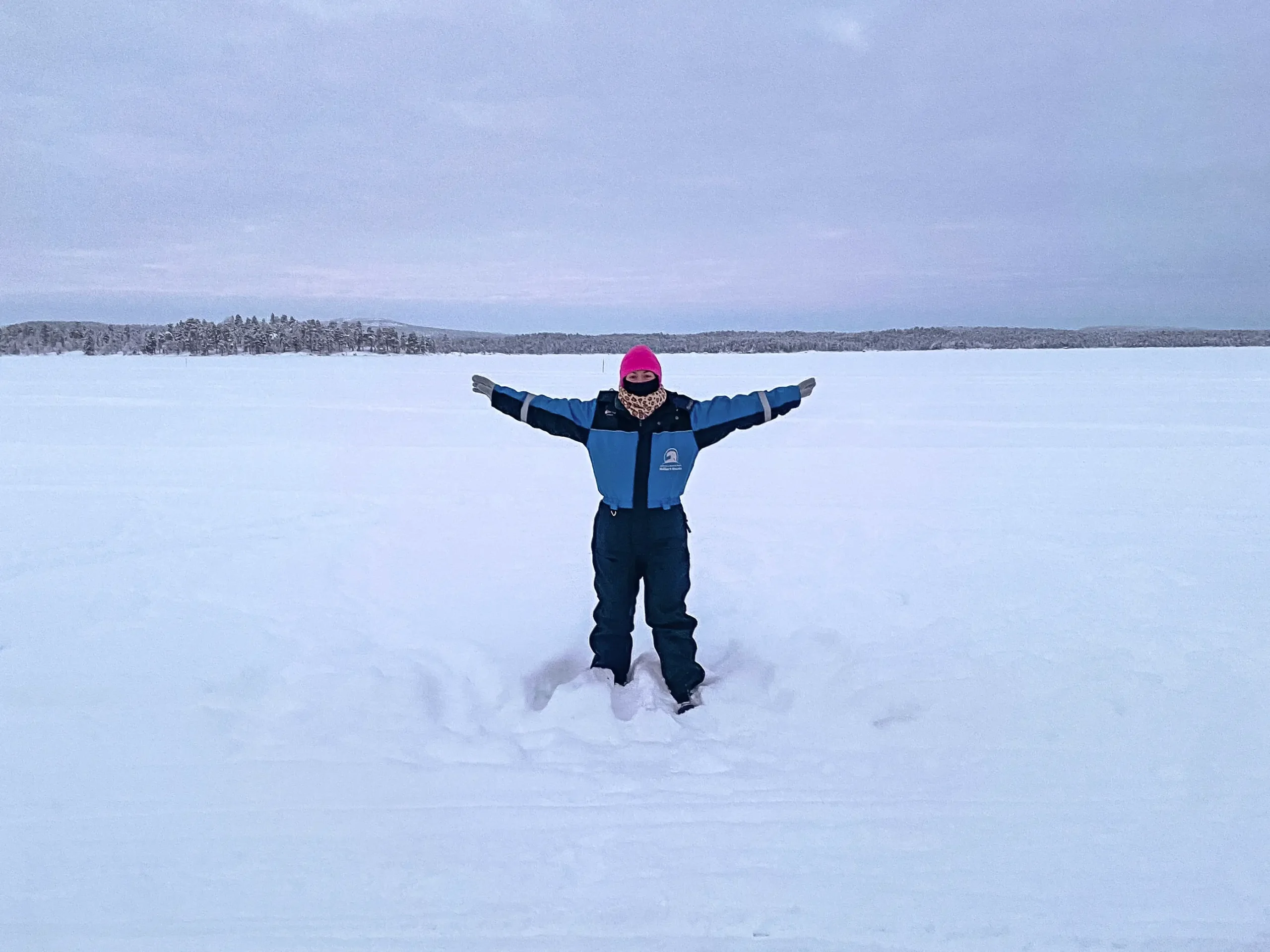 Solo traveller standing with arms outstretched on a snowy frozen lake in Finnish Lapland.