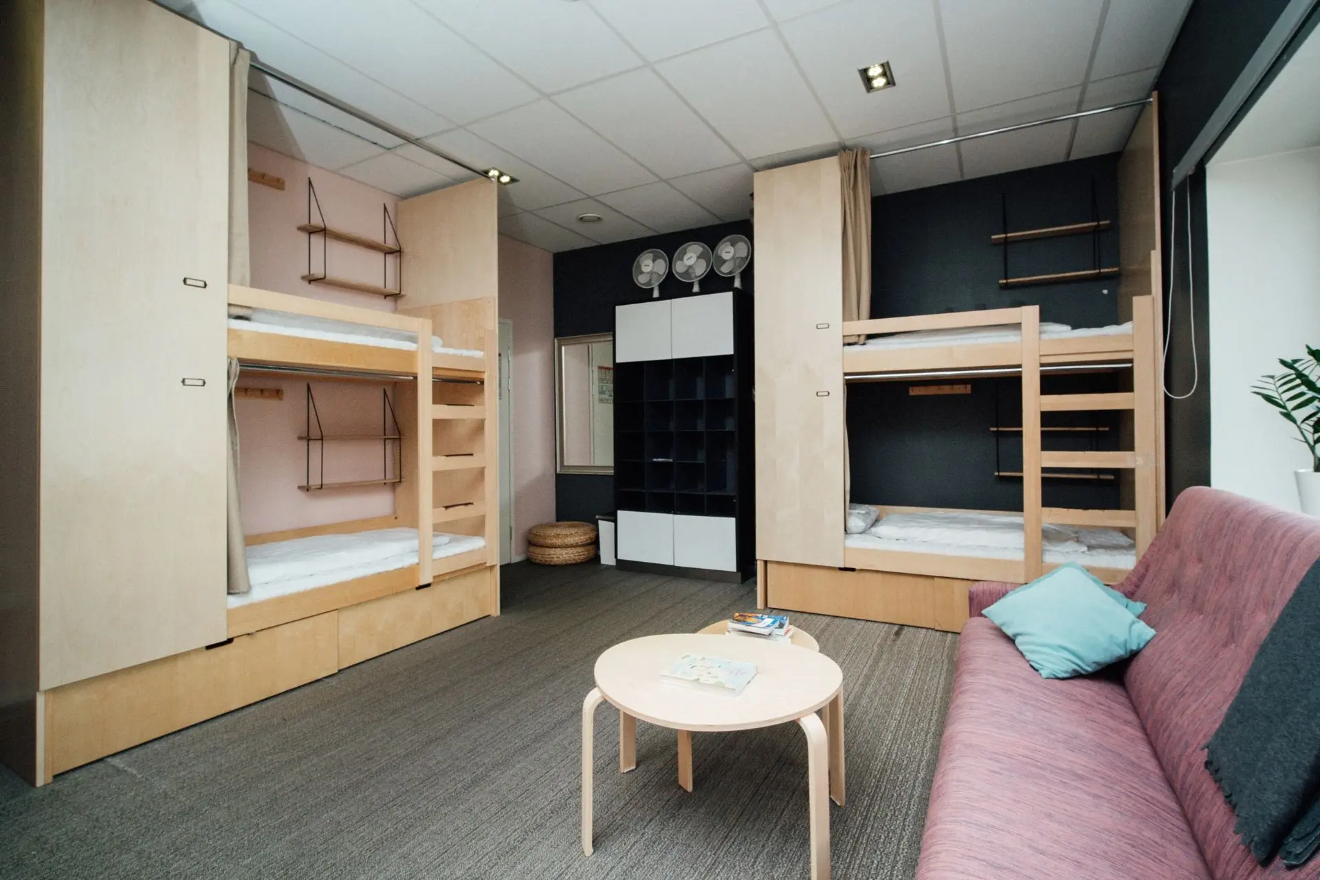 Shared room at The Yard Hostel in Helsinki with bunk beds, a sofa and small table.