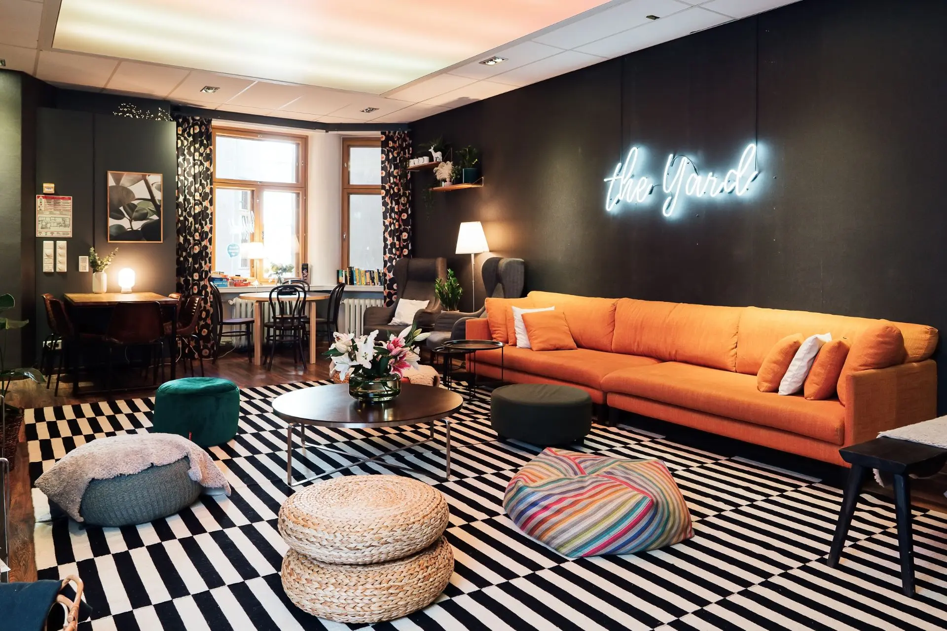 Cosy lounge at The Yard Hostel in Helsinki, with an orange sofa, patterned rug and colourful seating.