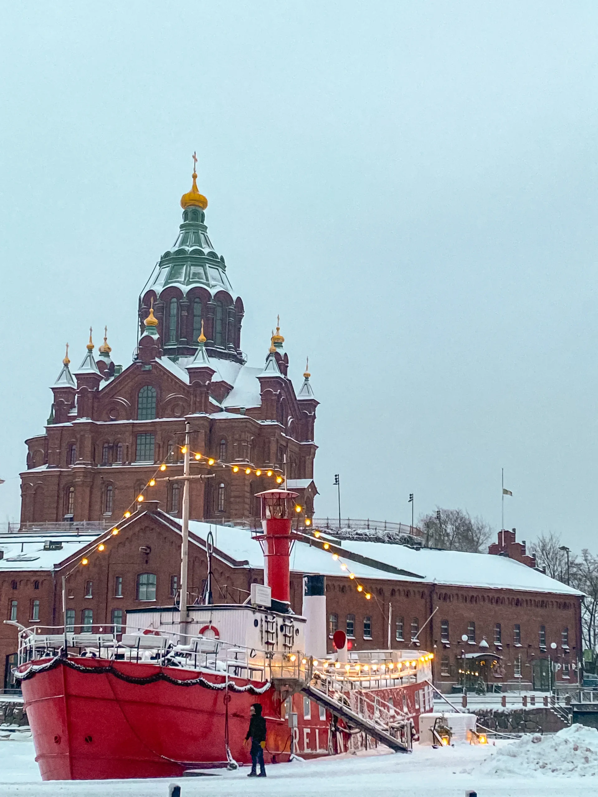 Snow-covered harbour in Helsinki with Uspenski Cathedral and a red icebreaker.