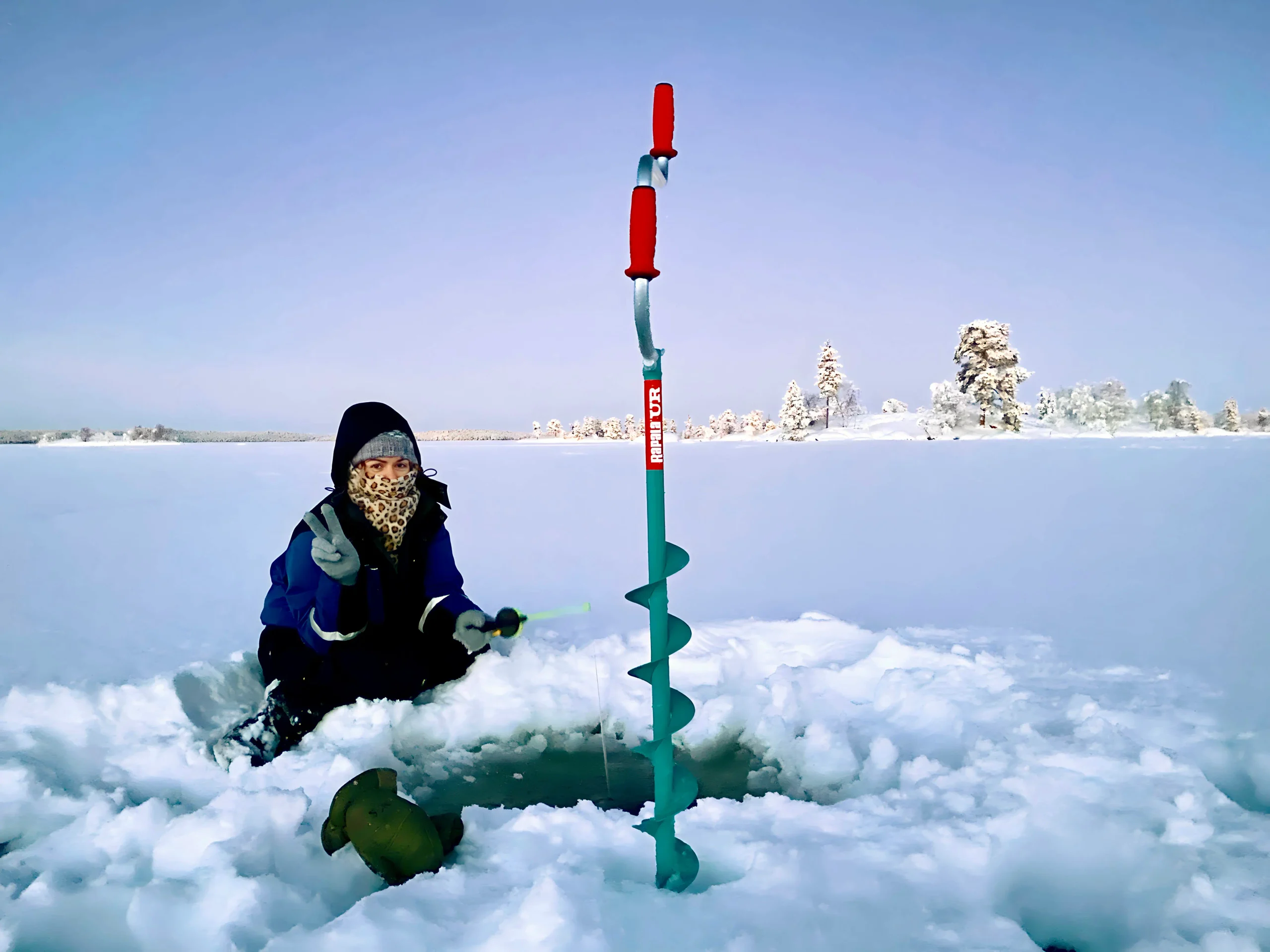 Woman in winter clothing ice fishing on a frozen lake in Finnish Lapland.