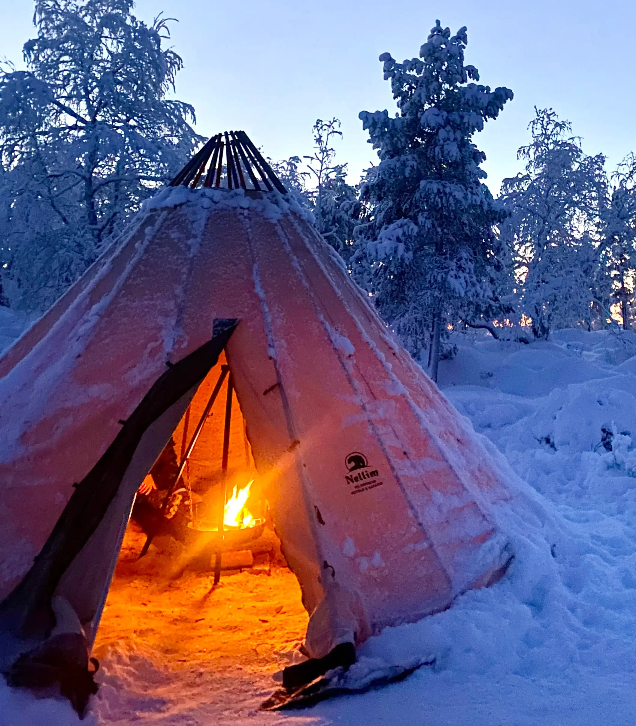 Snow-covered tipi with a fire burning inside