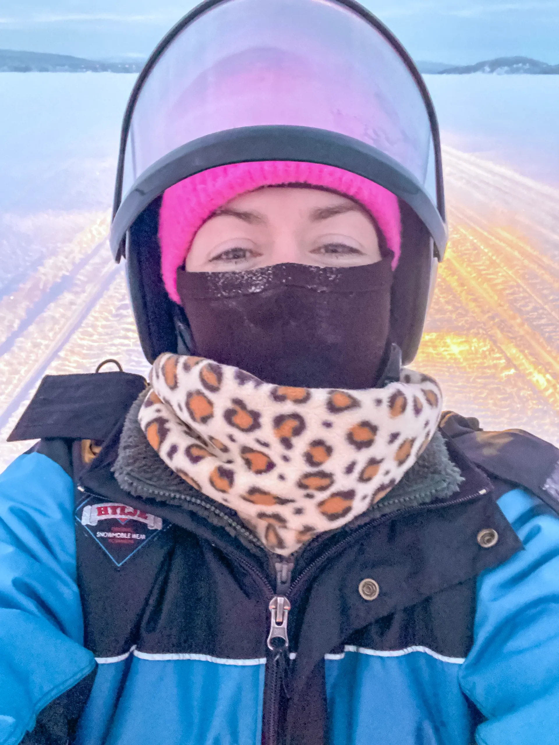 Woman dressed for a Lapland for adults adventure, wearing a blue winter jacket, pink hat and leopard-print snood.