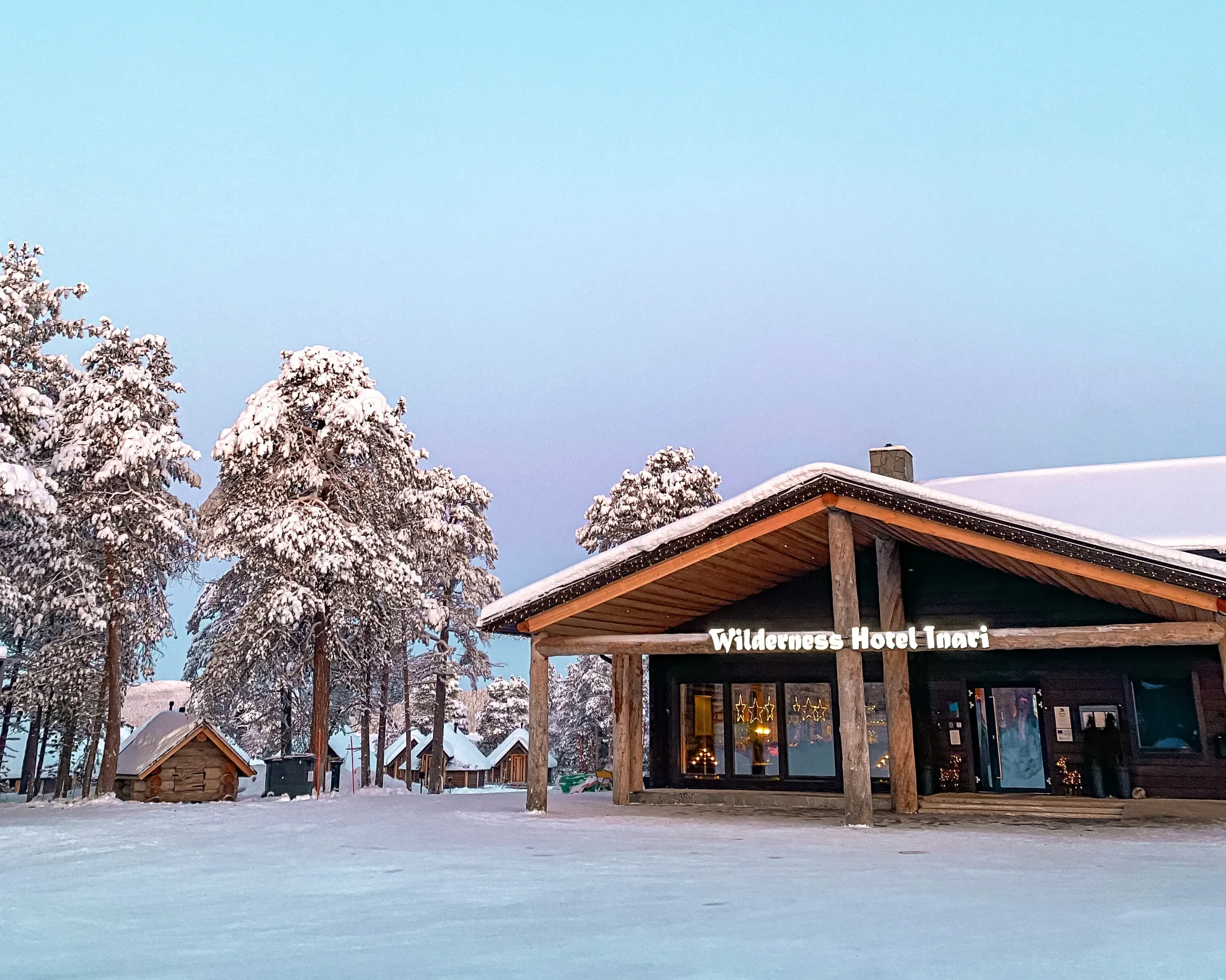 Wilderness Hotel Inari surrounded by snow-covered trees and cabins in Finnish Lapland.