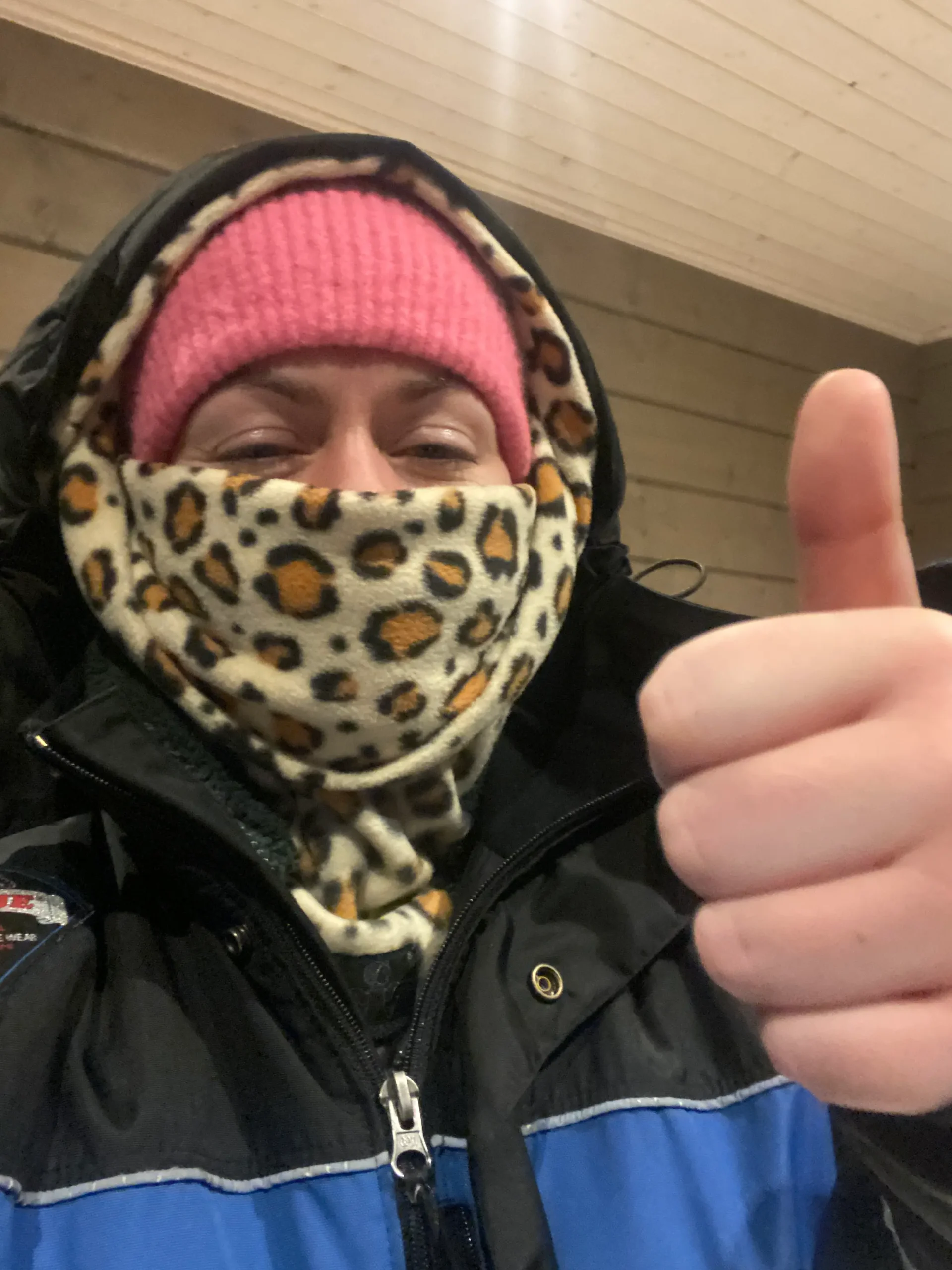 A woman wearing a leopard print snood, pink had and snowsuit in a Lapland hotel